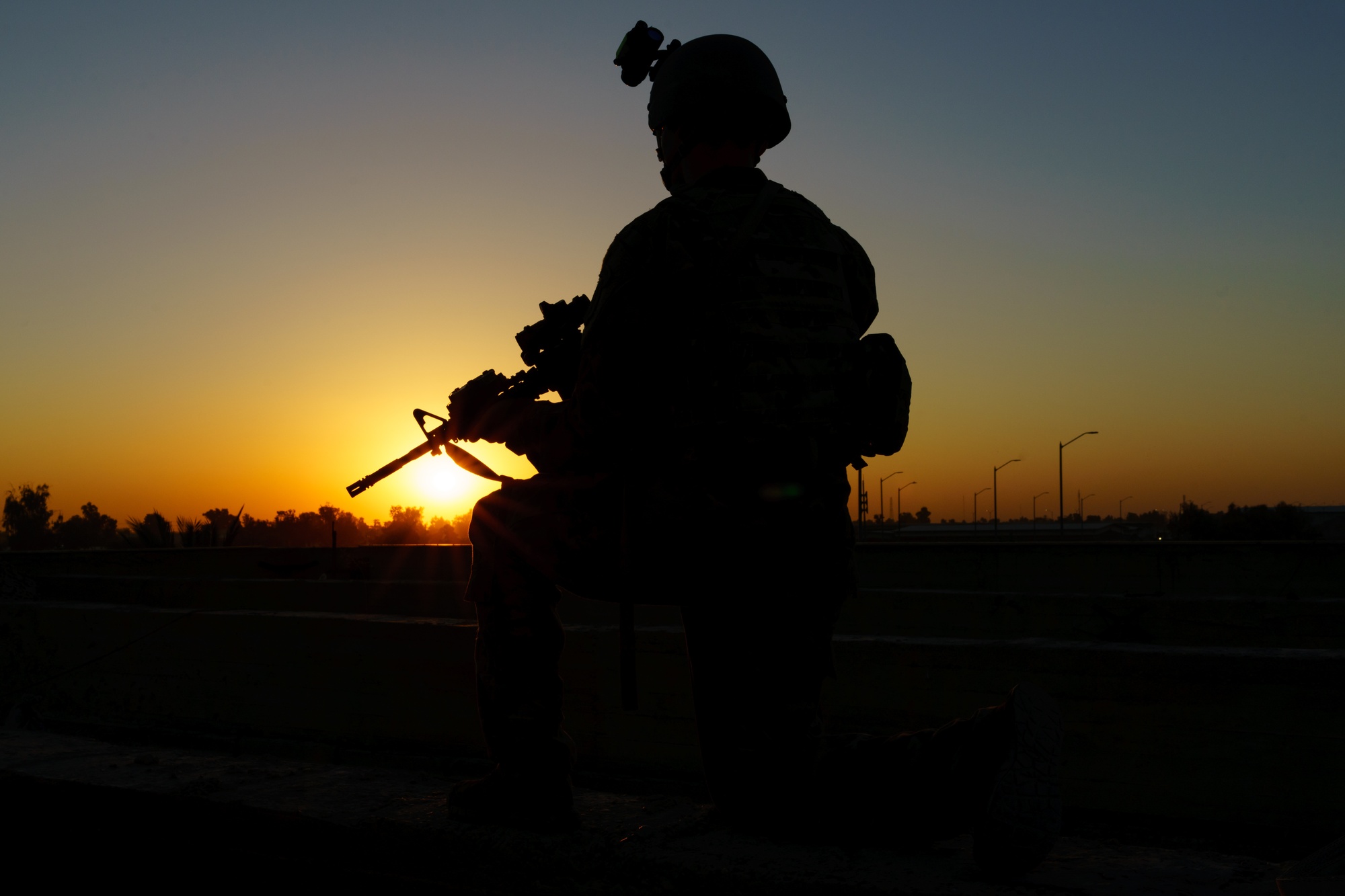 Special Forces soldier silhouetted at a machine gun against a sunset sky
