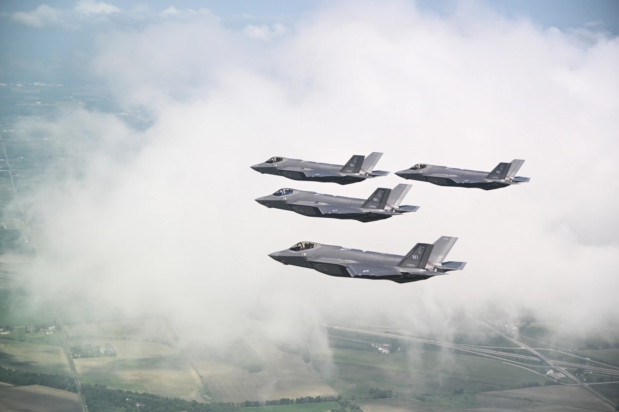 Two F-35 Lightning II fighters in formation flight through layered clouds, seen from below